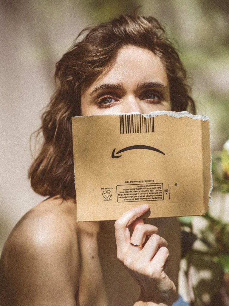 A woman holds up an Amazon box, but the Amazon smile is upside down