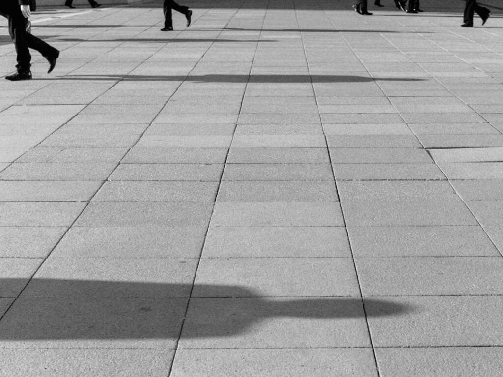 Black and white image of feet and shadows walking across a concourse. 